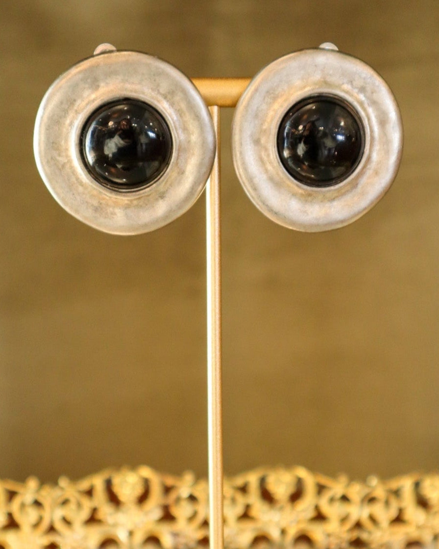 Pair of gold earrings on a stand with a reflective surface and decorative background