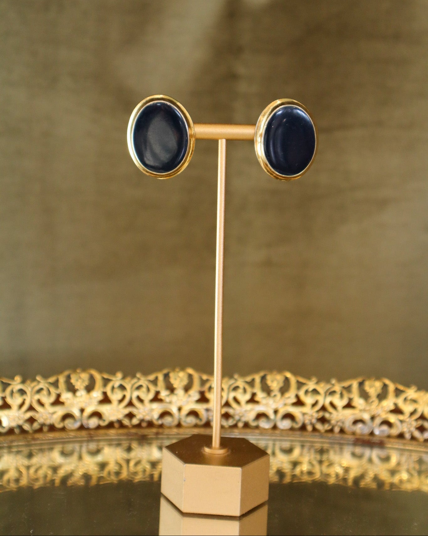 Pair of gold-framed earrings with black stones on a gold stand against a gold background
