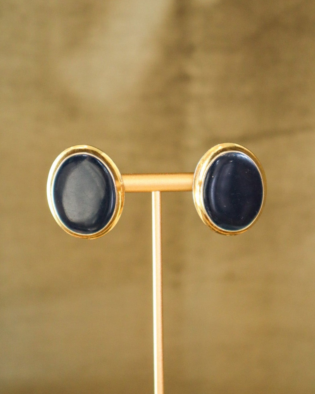 Pair of gold-framed earrings with black stones on a gold stand against a gold background