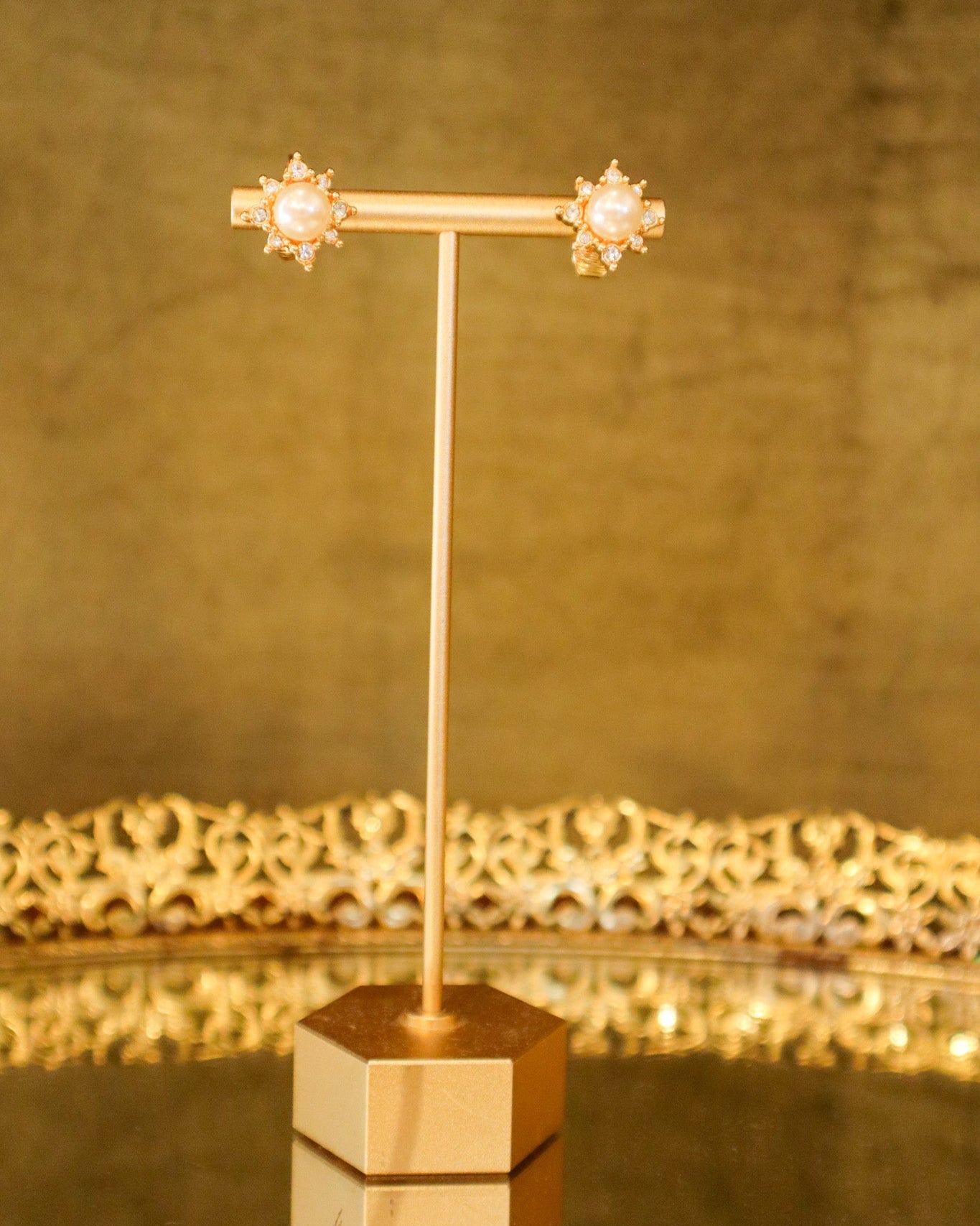Gold earrings with pearl-like centers on a gold stand against a matching background