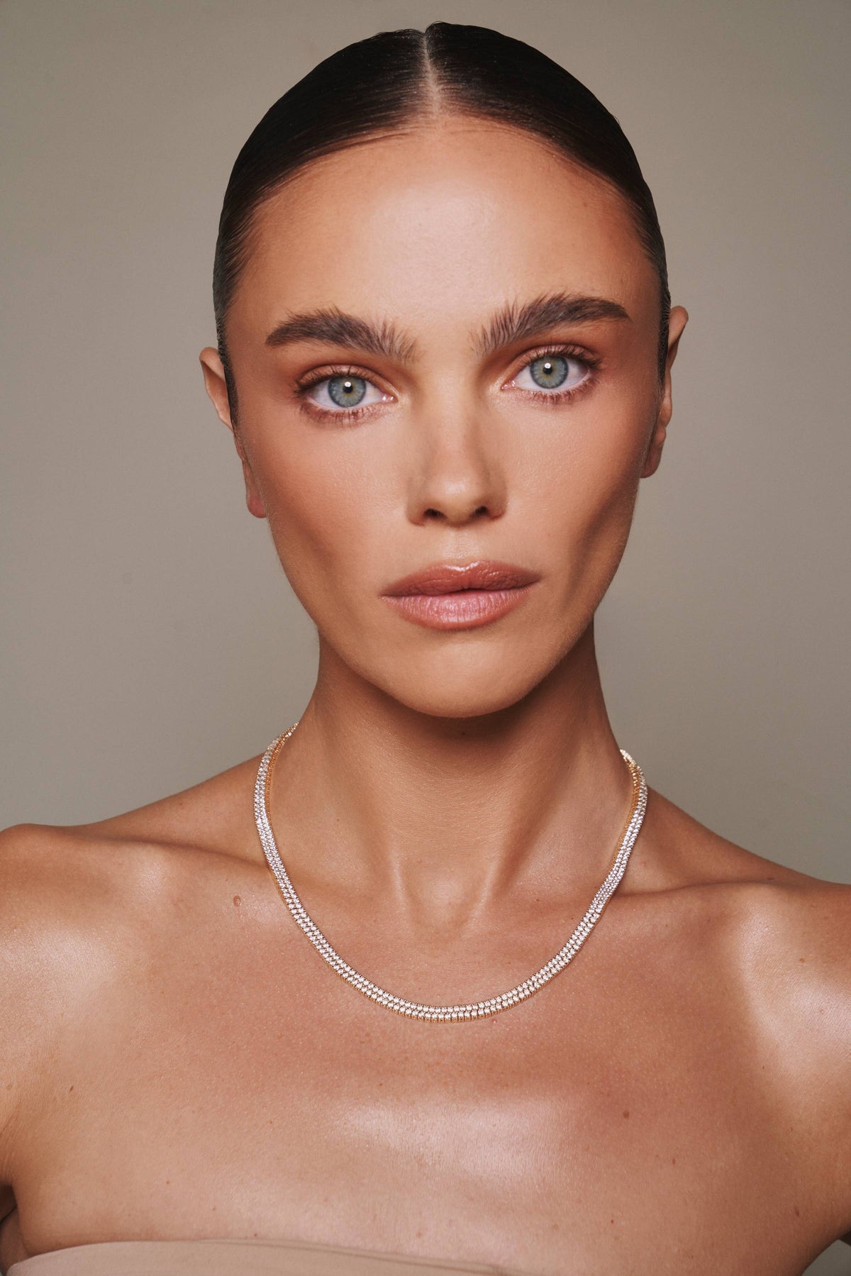 Woman wearing a silver necklace against a neutral background